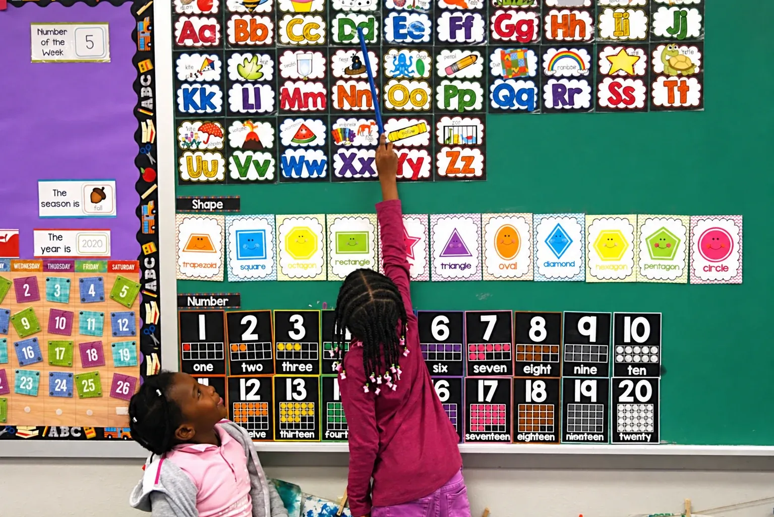 A preschooler reaches up to point at the alphabet wall