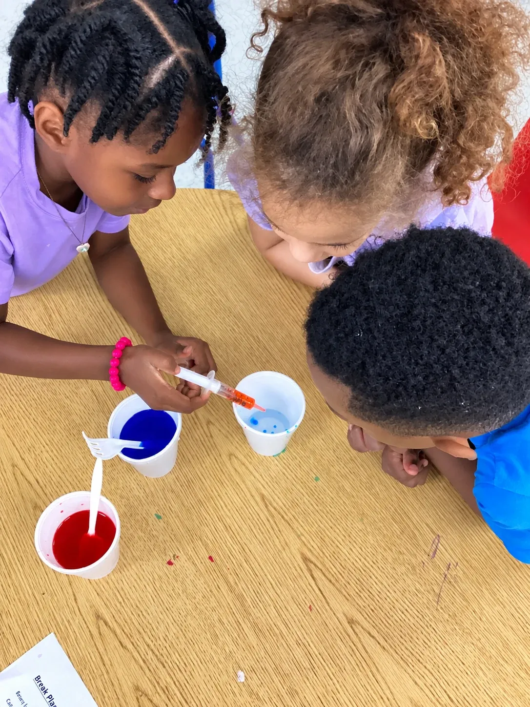 Three preschoolers lean in to watch colors mix during a science activity