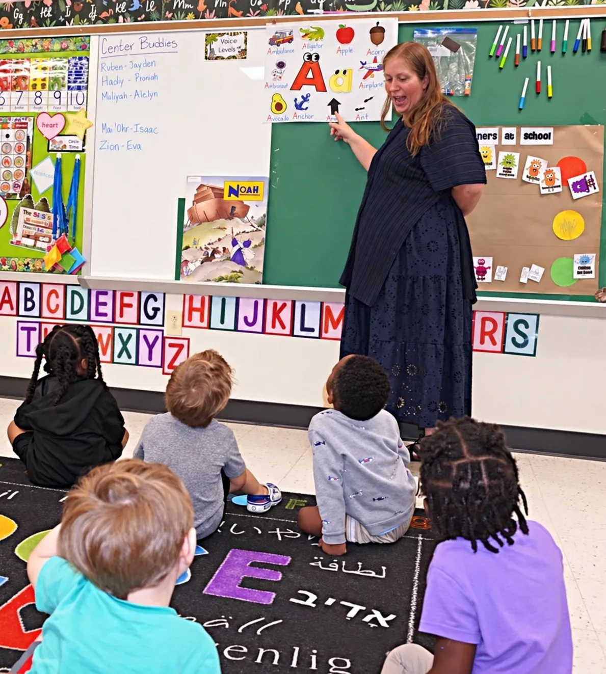 A teacher points to an alphabet chart while preschoolers sit on the rug for circle time at Chapel Glen Early Learning Academy