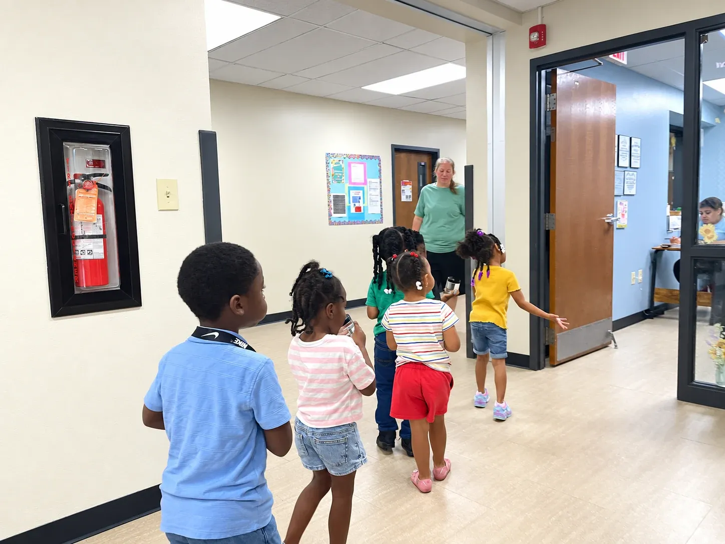 A line of preschoolers walks down the hallway to their classroom