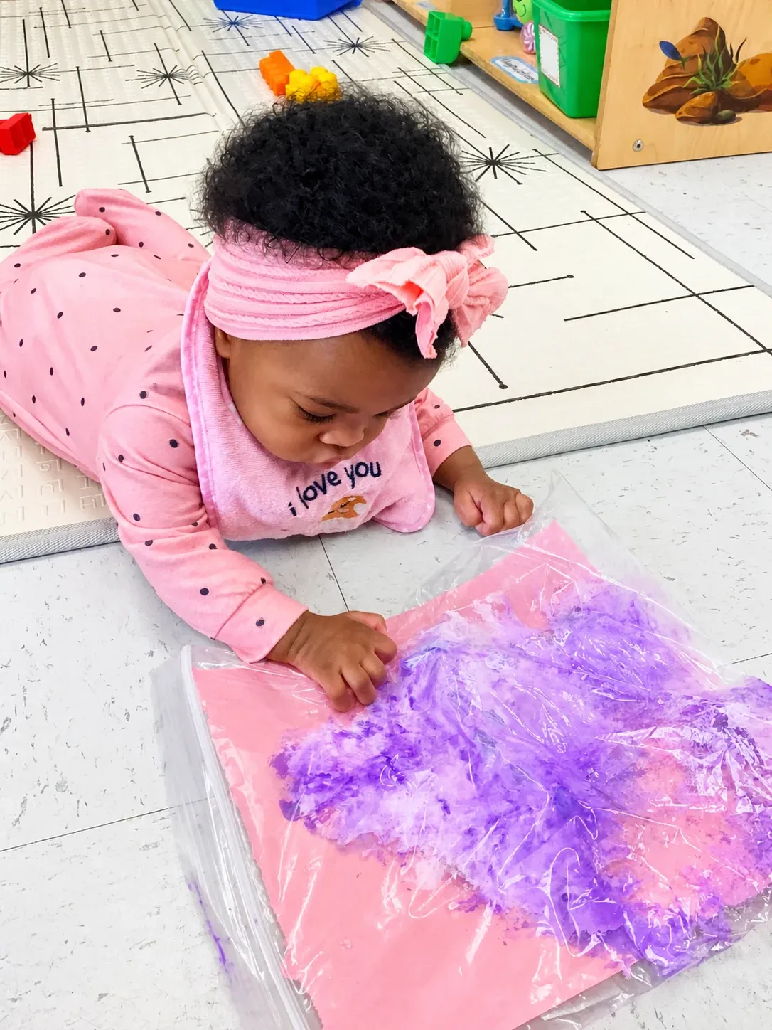 An infant explores purple paint with her hands