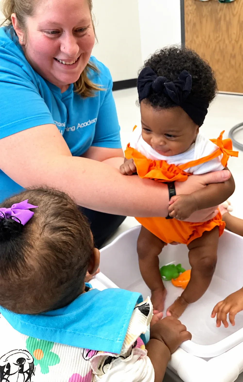 A teacher helps an infant splash in a water tub