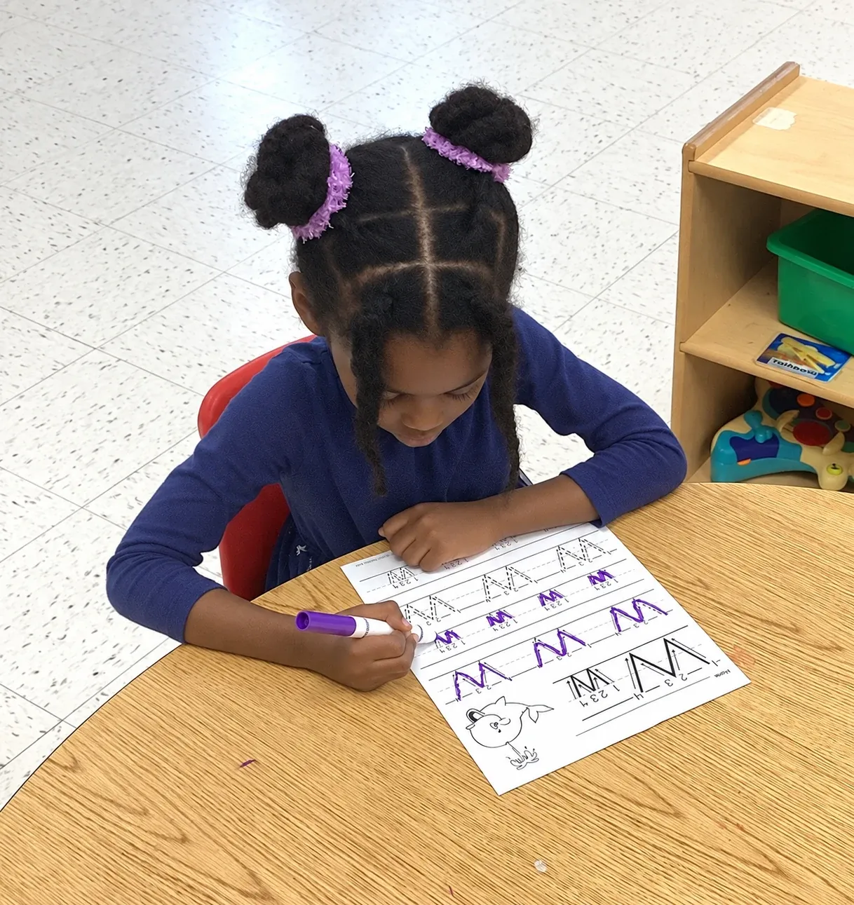 A preschooler traces the letter M on a worksheet