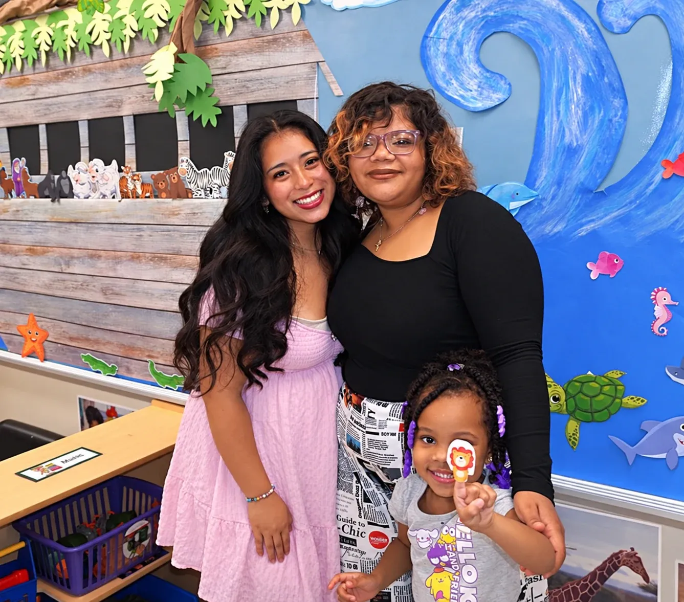 Two teachers and a student pose in front of the Noah's Ark classroom mural