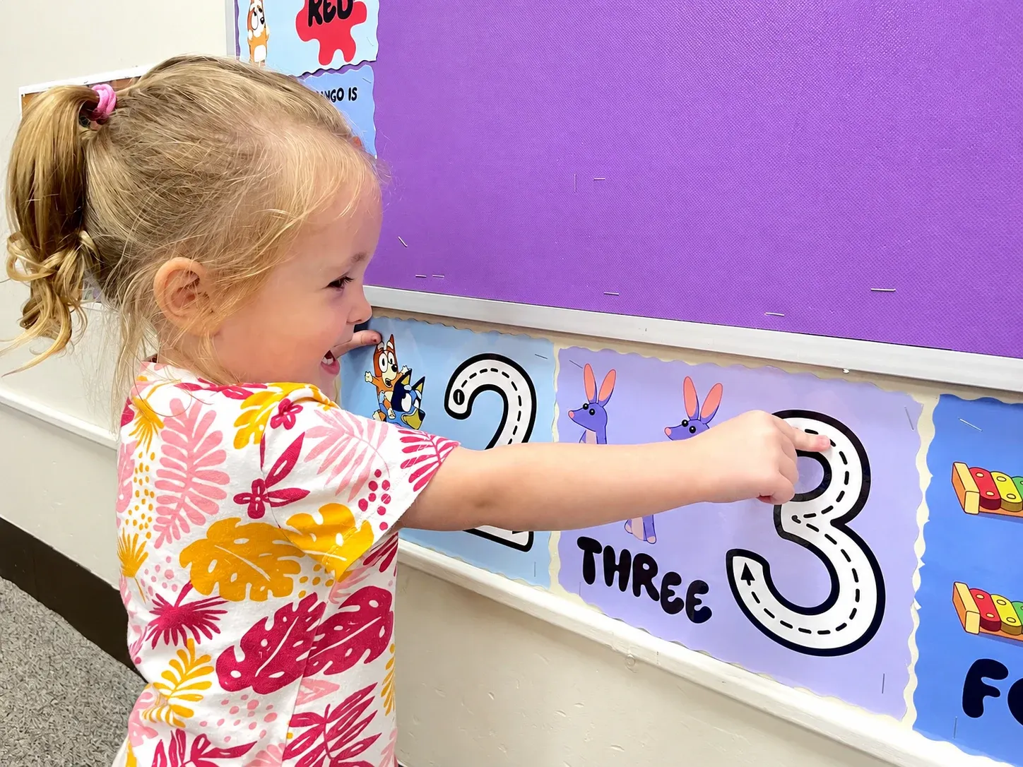A toddler points at the number three on the classroom number wall