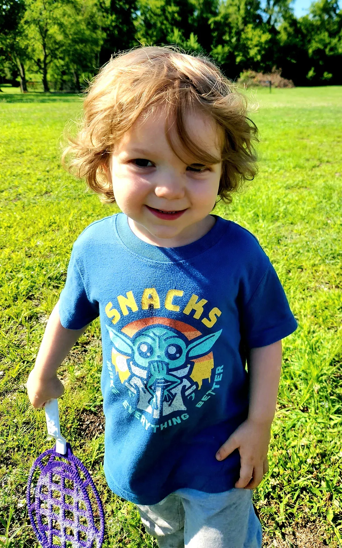 A boy holds a racket on the grassy field outside
