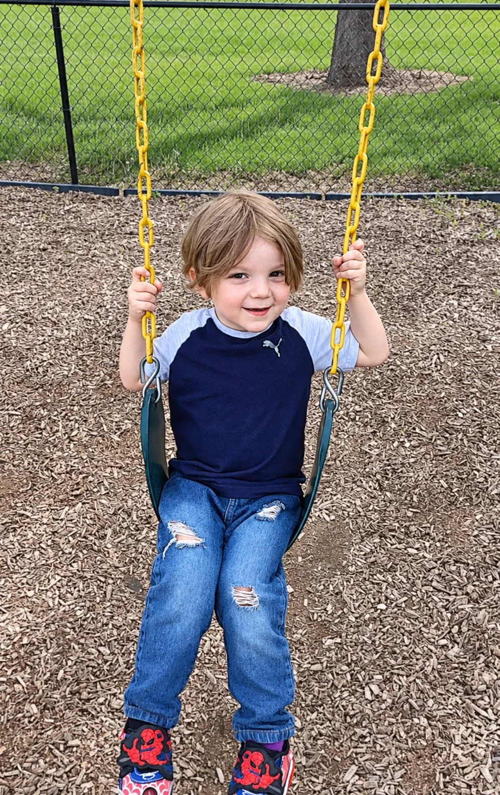 A smiling boy on a swing at the playground