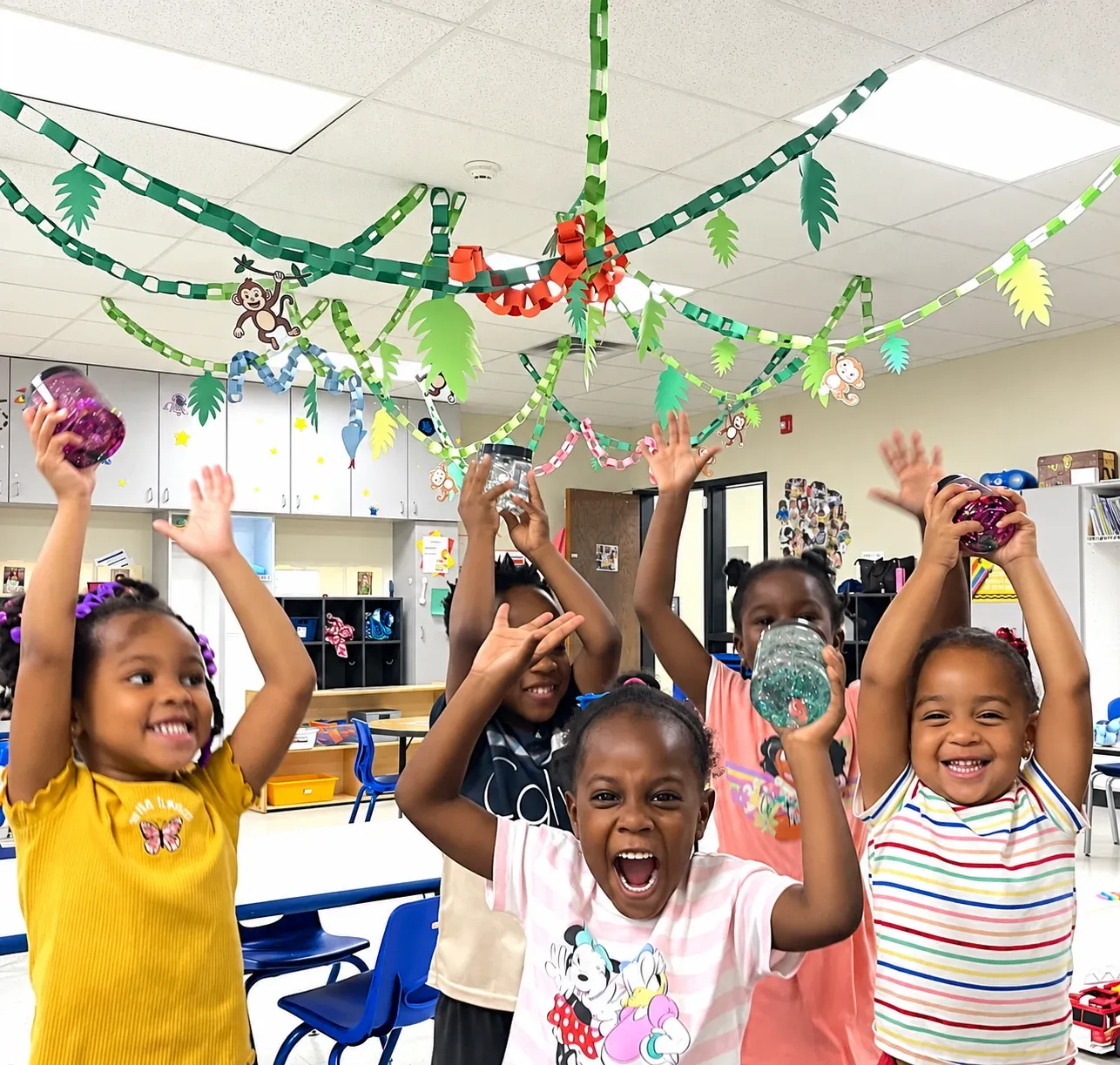 Preschoolers throw their hands in the air and cheer under a paper jungle canopy