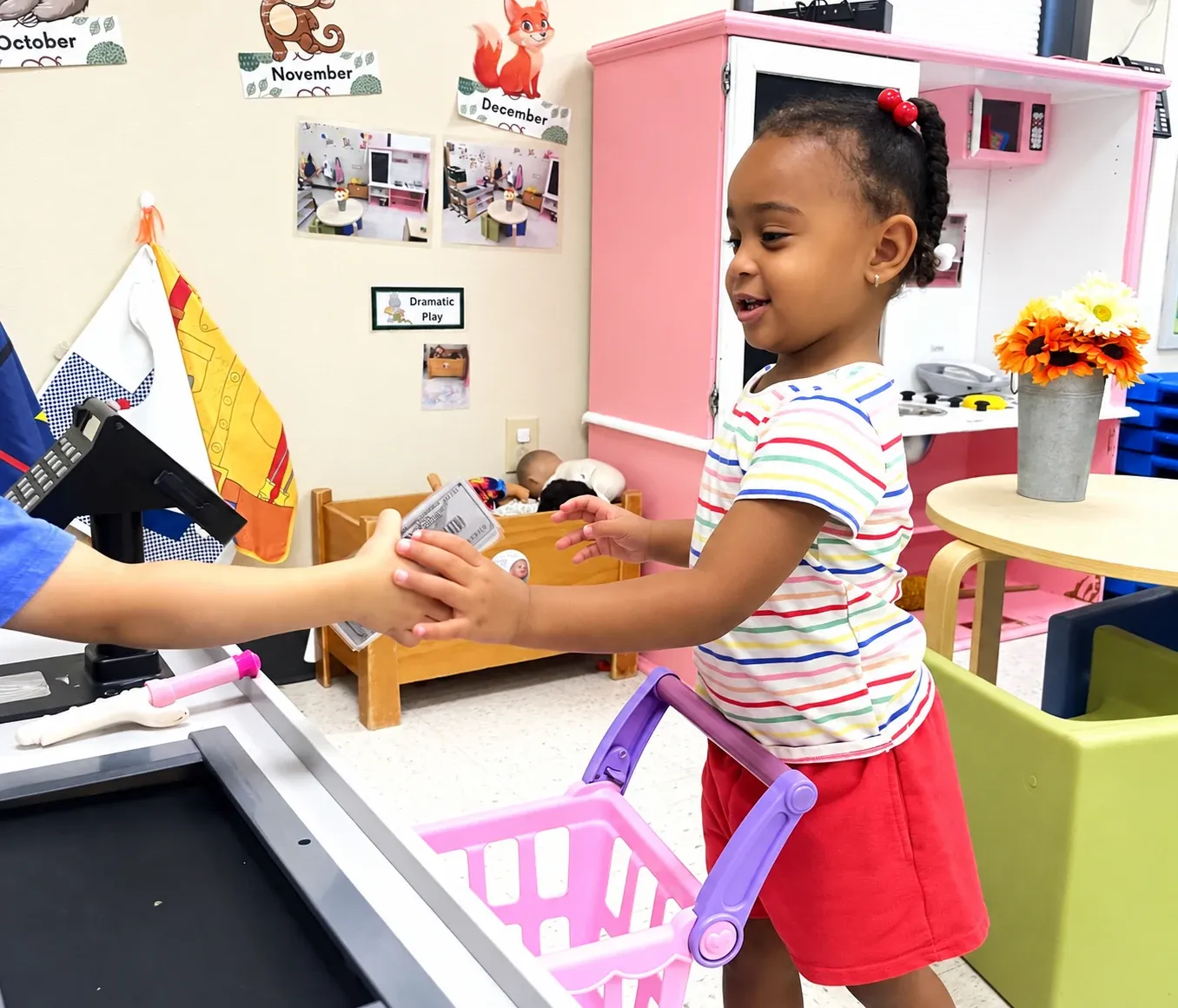 A toddler pays at the pretend grocery checkout in the dramatic play center