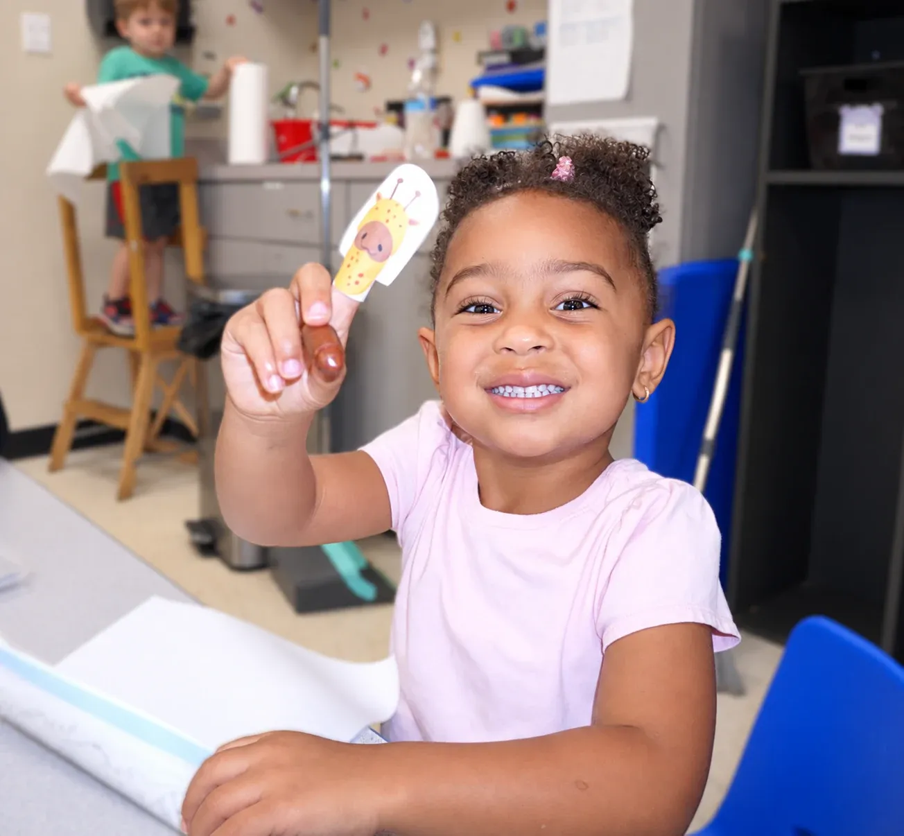 A girl smiles while holding up a finger puppet