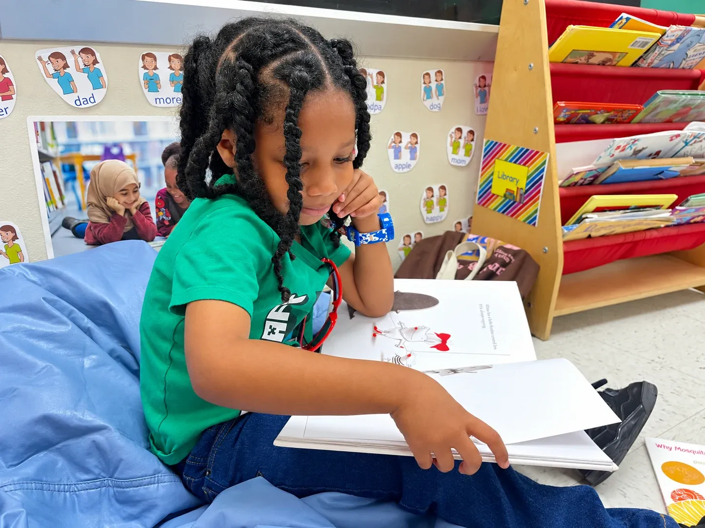 A preschooler reads a picture book in the classroom library corner