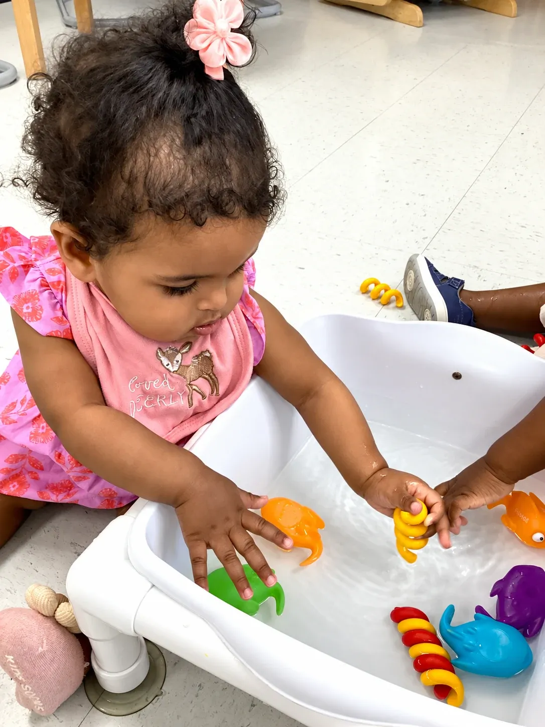 A toddler plays with rubber sea creatures at the water table