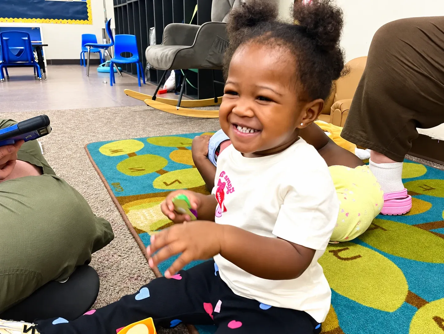 A toddler laughs on the classroom rug during circle time