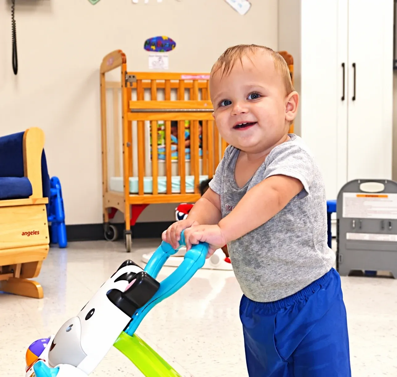 A toddler pushes a walker toy across the infant room