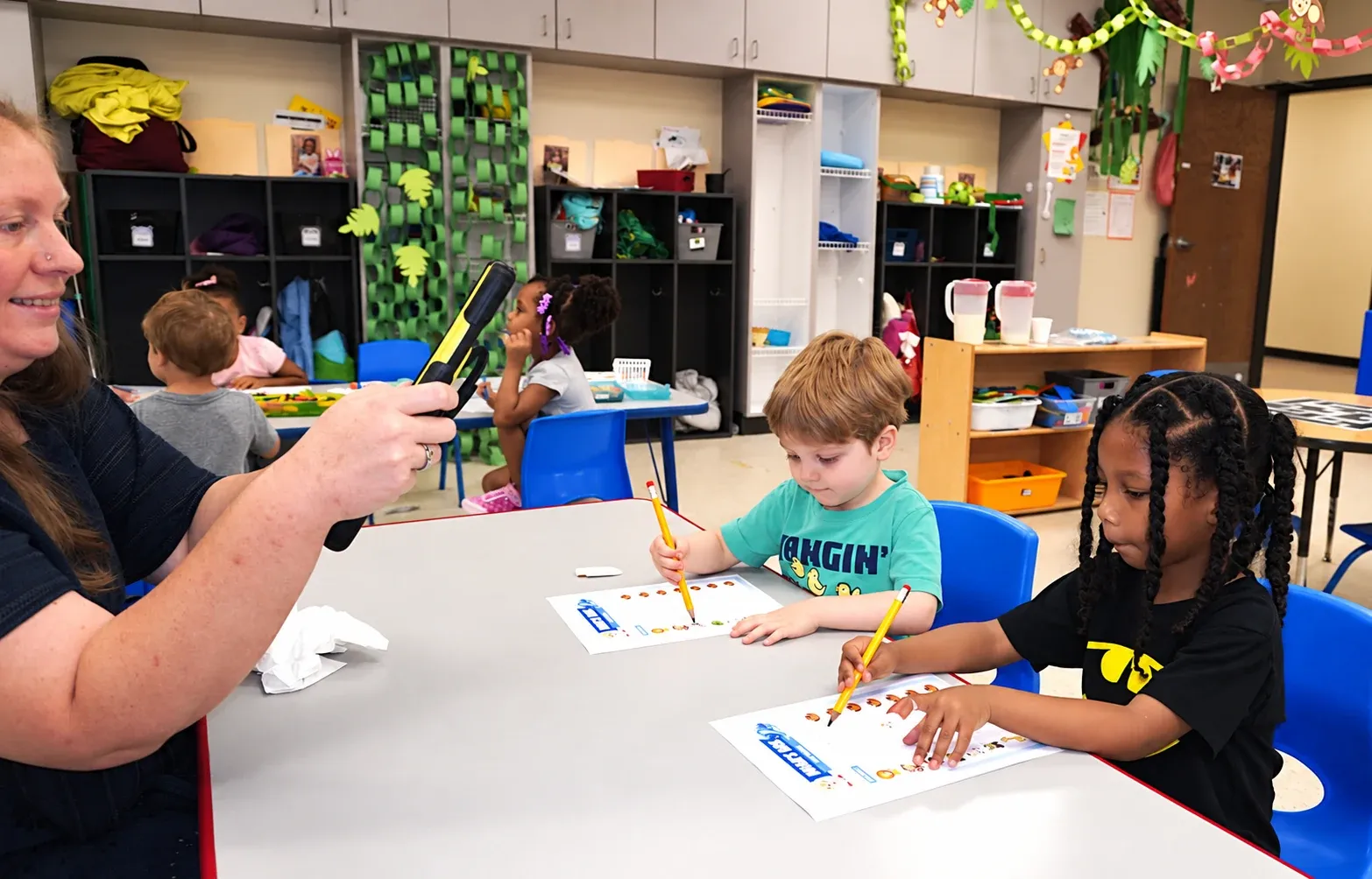 Preschoolers work on tracing worksheets with their teacher